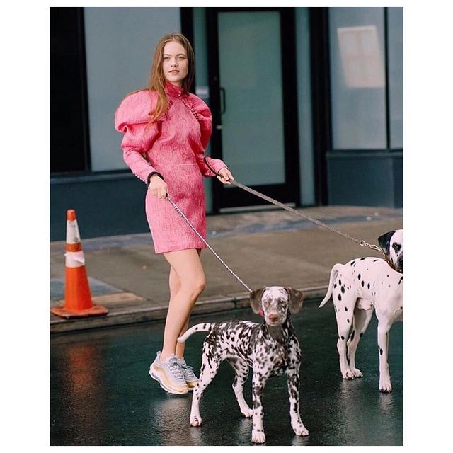 Hera Hilmar in a pink one piece with her black spotted white dogs.
